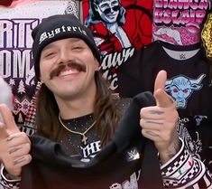 a man with long hair wearing a hat and holding up two thumbs