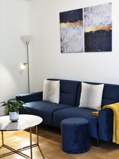 a living room with a blue couch and two paintings on the wall