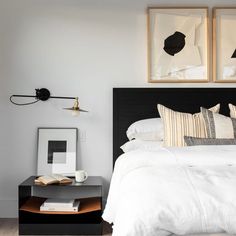 a bed with white sheets and pillows in a bedroom next to two pictures on the wall