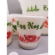 there are four cups and two spoons on the table together, one is red and white with green lettering