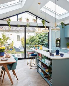 an open kitchen with skylights above the island and table in front of it, surrounded by potted plants