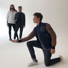 three men standing in front of a white background with one man holding his leg up