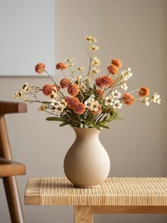 a vase filled with lots of flowers sitting on top of a wooden table next to a chair