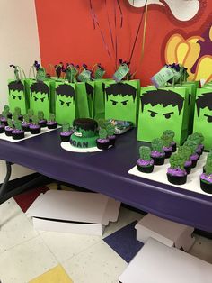 a table topped with cupcakes covered in green frosting and hulk face bags