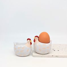 two ceramic chickens in a bowl with an egg