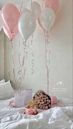 pink and white balloons are hanging from the ceiling above a bed, with a gift bag on it