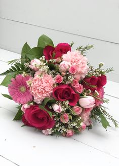 a bouquet of pink and red flowers sitting on top of a white table next to a wall