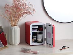 a red and white mini fridge sitting on top of a table next to a brush