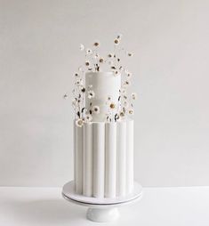 a three tiered white cake with daisies on top, sitting on a pedestal