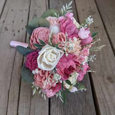 a bridal bouquet with pink and white flowers sits on a wooden floor, ready to be used as a bride's bouquet