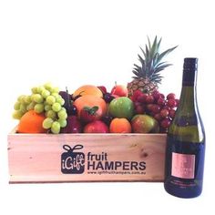 a wooden box filled with lots of fruit next to a bottle of wine and a pineapple