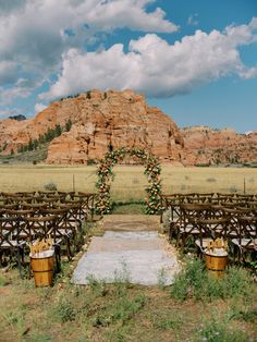 an outdoor ceremony set up with wooden chairs and flowers on the aisle, in front of a large rock formation