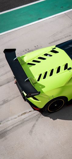 a lime green sports car driving down a race track with its hood up and the door open