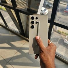 a hand is holding a remote control in front of a glass window that looks out onto the street