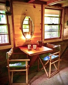 two chairs and a table in a room with wood paneling on the walls, along with a round mirror