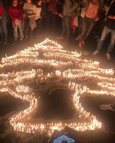 a group of people standing in front of a large number of lit candles on the ground