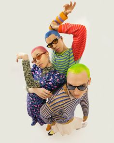 three people with colorful hair and sunglasses are posing for the camera while one person holds his arm up in the air