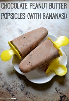 two pieces of chocolate peanut butter popsicles on a white plate with yellow spoons