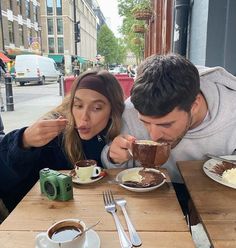 a man and woman sitting at a table eating cake with coffee in front of them