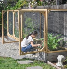 a woman kneeling down in front of a chicken coop with plants growing out of it