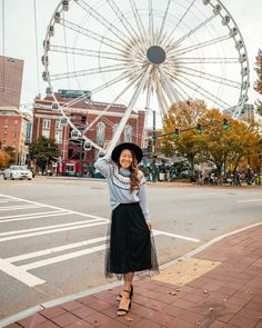 a woman is standing on the sidewalk in front of a ferris wheel