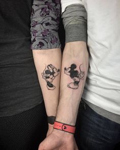 two people holding hands with mickey and minnie mouse tattoos on their arms, both wearing matching wristbands