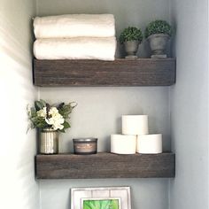 two wooden shelves with towels, candles and pictures on them in a bathroom area next to toilet paper rolls