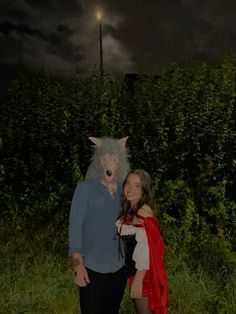 two people standing next to each other in front of bushes with a wolf mask on