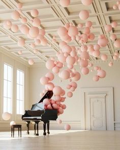 a piano is surrounded by balloons floating from the ceiling in an empty room with white walls