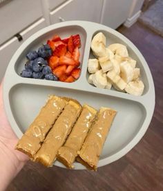 a person holding a plate with peanut butter, fruit and crackers on it in their hand