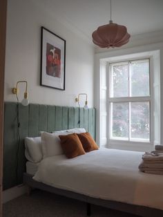 a bed with white sheets and pillows in front of a window next to a painting on the wall