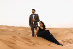 a man standing next to a woman on top of a sand dune in the desert