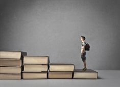 a young boy standing on top of a stack of books in front of a gray background