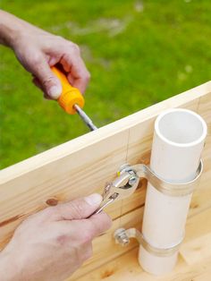 two hands are working on a piece of wood that is attached to a fence post