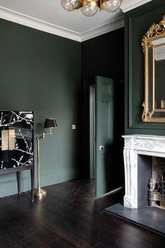 an empty room with green walls and wood floors, a mirror on the wall and a fireplace in the corner