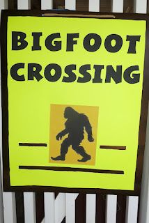 a bigfoot crossing sign is posted on the side of a white fence with black lettering