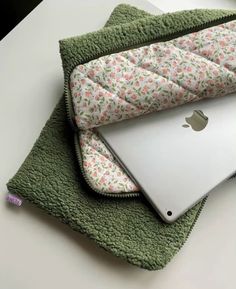 an apple laptop computer sitting on top of a green towel next to a pillow and blanket