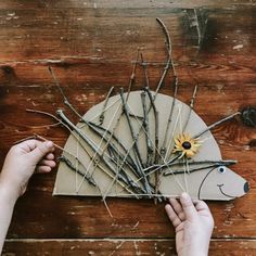 two hands are working on an animal head made out of sticks and twigs with a sunflower in the center