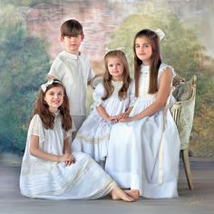 three children in white dresses sitting on a chair