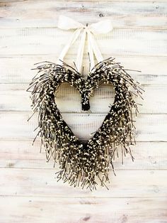 a heart shaped wreath with black and white sprigs hanging from the side on a wooden wall