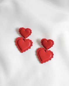 two red heart shaped earrings sitting on top of a white sheet