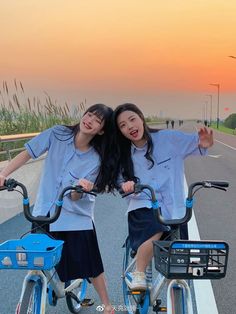 two girls are riding bicycles on the road at sunset or sunrise with their arms around each other