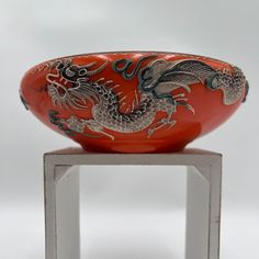 a red and black dragon bowl sitting on top of a metal stand in front of a white background