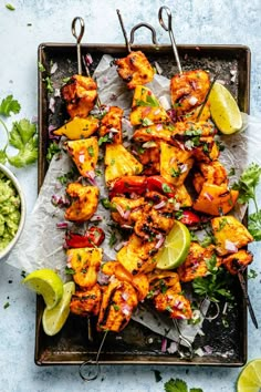 chicken skewers with pineapples and cilantro on a tray next to guacamole