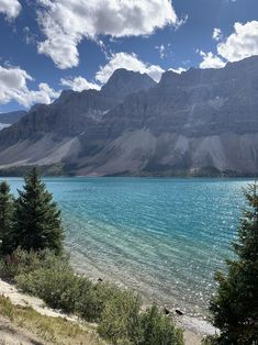 a lake surrounded by mountains and trees in the foreground with blue water on either side