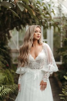 a woman in a white wedding dress posing for the camera with her hands on her hips