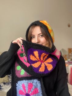 a woman wearing a colorful crocheted scarf and holding up a knitted bag