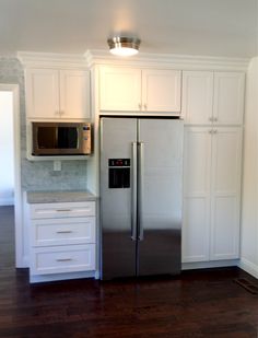 a silver refrigerator freezer sitting inside of a kitchen next to white cabinets and drawers