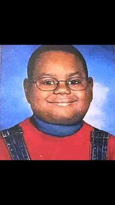 an image of a man with glasses and a red shirt smiling at the camera in front of a blue background