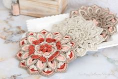 three crocheted flower coasters sitting on top of a marble table next to a book